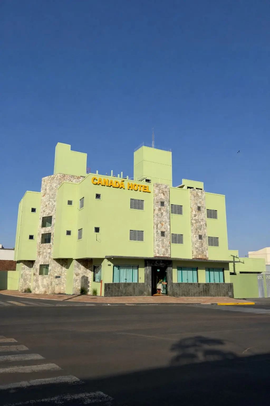 Fachada do Canadá Hotel em Rio Verde, prédio verde-claro com pedra e letreiro amarelo sob céu azul
