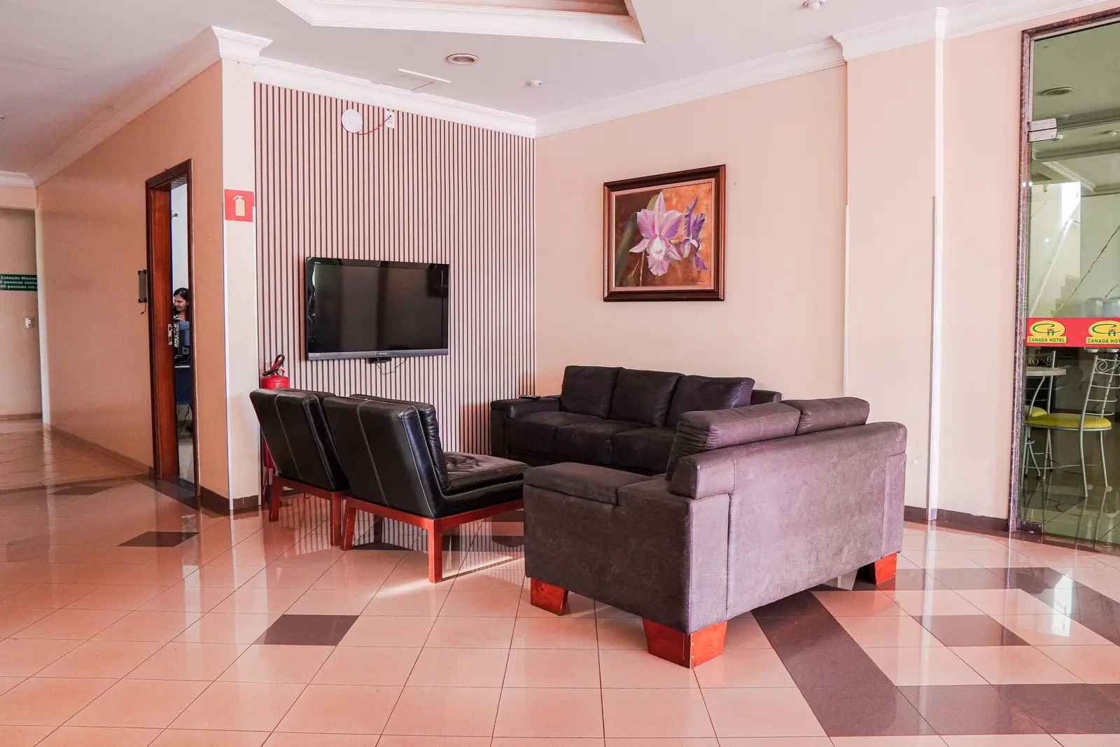 Lobby com sofás marrons, poltronas e TV de parede