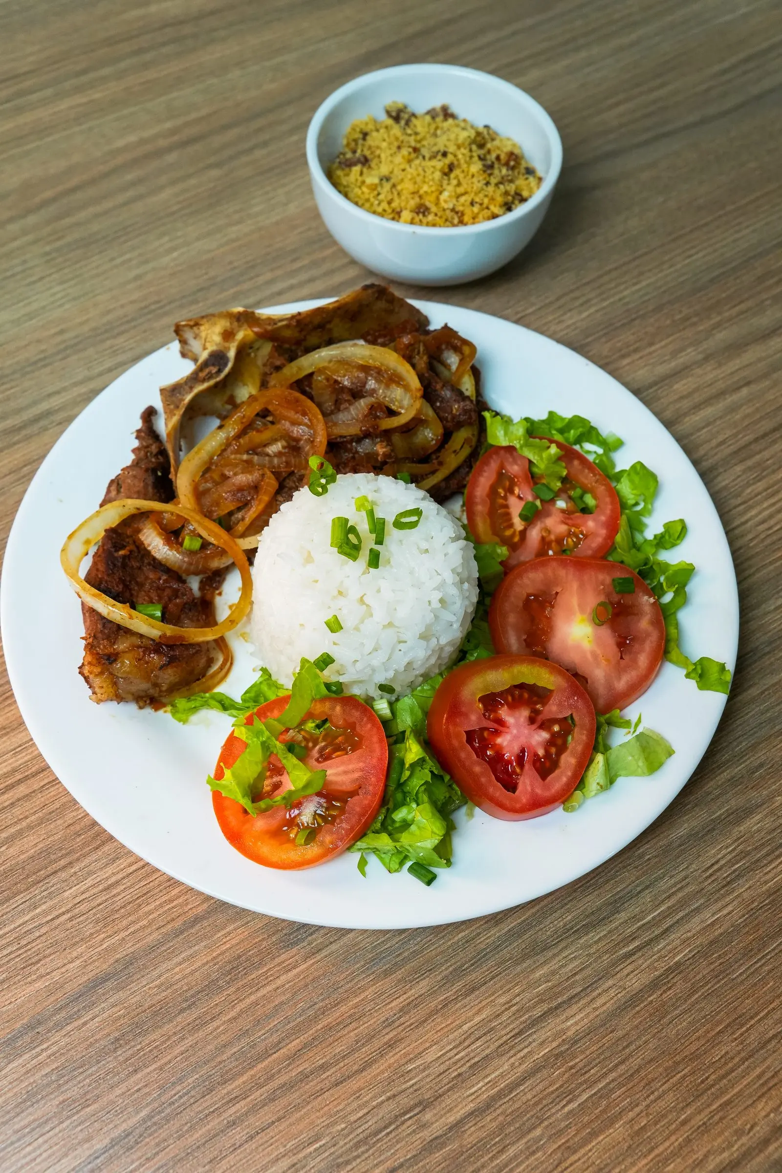 Prato com bisteca acebolada, arroz, salada de tomate e farofa