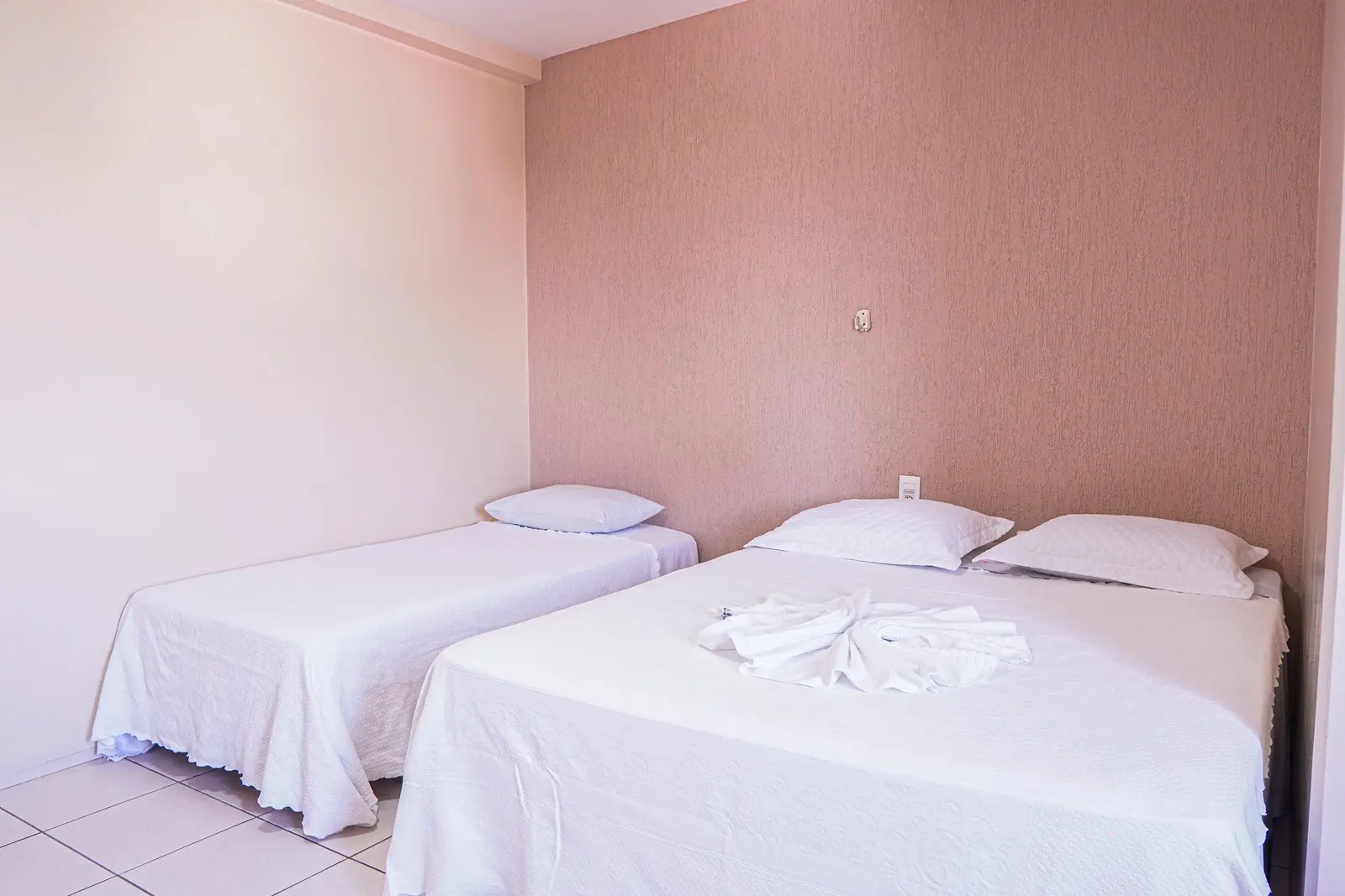 Quarto Triplo com camas alinhadas e paredes em tom rosado
